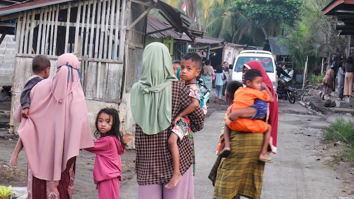 Des femmes et des enfants marchent dans une rue d'un village.