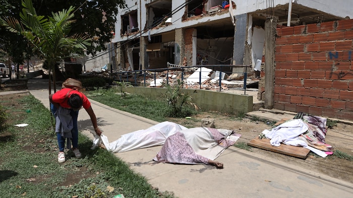 Un homme regarde des corps recouverts d'un drap blanc devant un bâtiment endommagé, au lendemain des séismes et de plusieurs répliques qui ont frappé La Guaira, au Venezuela, le jeudi 25 juin 2026.