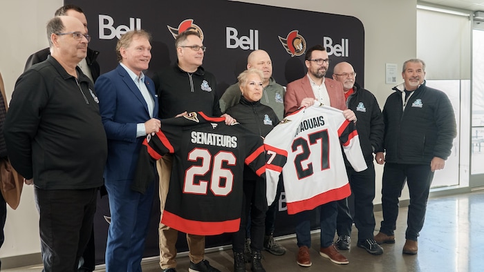 Des personnes présentent des chandails de hockey aux couleurs des Sénateurs d'Ottawa.