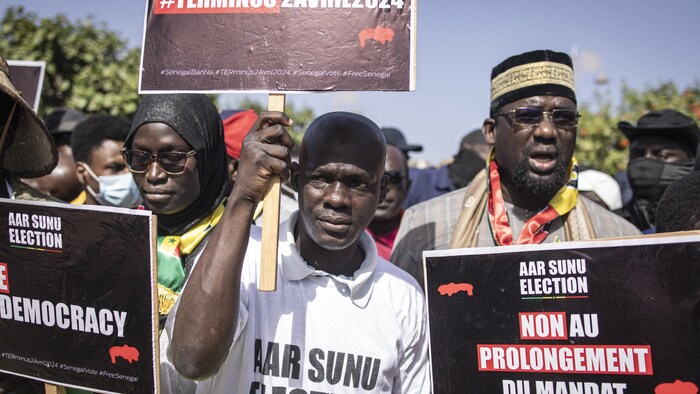 Des personnes tiennent des pancartes lors d'un rassemblement. 