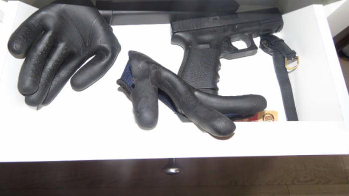 Une arme de poing de type Glock 19 et des gants noirs dans un tiroir.