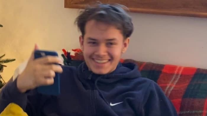 Une photo de Jonathan Adamski souriant sur un sofa avec son chien sur les genoux.