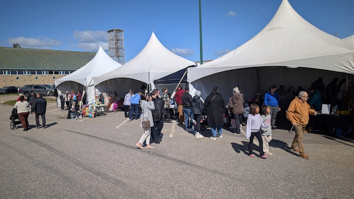 Plusieurs grands chapiteaux blancs sont alignés. Des personnes se promènent et visitent les stands.