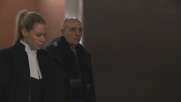 Serge Audette marche dans un corridor d'un palais de justice à côté de son avocate.
