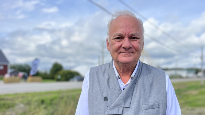 Un homme en chemise pose devant une ferme.