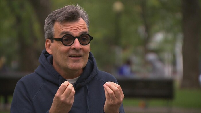 Un homme portant un coton ouaté noir, avec des lunettes rondes noires.