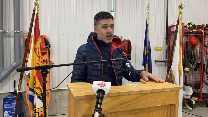 Serge Cormier parle, debout à un lutrin installé dans une caserne de pompiers.