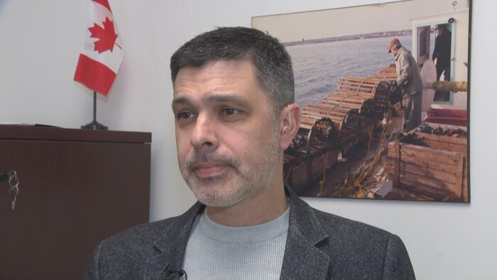 Un homme en entrevue, un cadre représentant un pêcheur de homard derrière lui.