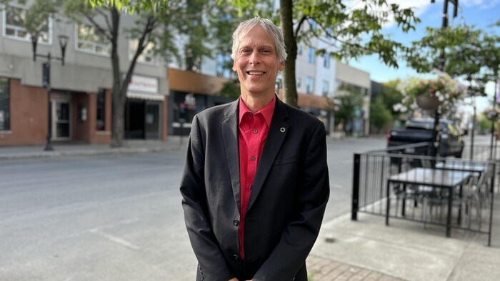 Serge Gauthier sourit à la caméra en prenant la pose sur un trottoir du centre-ville de Rouyn-Noranda.