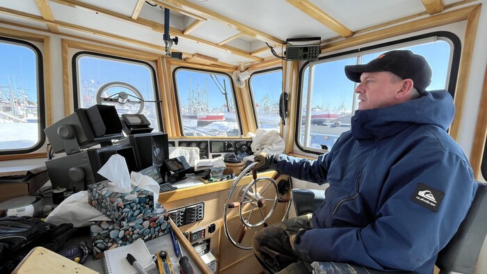 Serge Poirier tient le gouvernail à l'intérieur de la cabine de pilotage de son bateau. 
