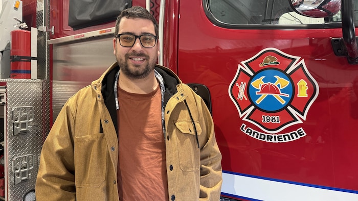 Guillaume Lacasse sourit à la caméra en posant près d'un camion de pompiers de Landrienne.