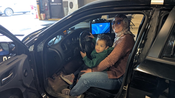 Un enfant qui fait semblant de conduire une voiture de police, assis sur les genoux d'une dame.