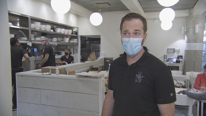 Un homme masqué devant la salle à manger d'un restaurant.