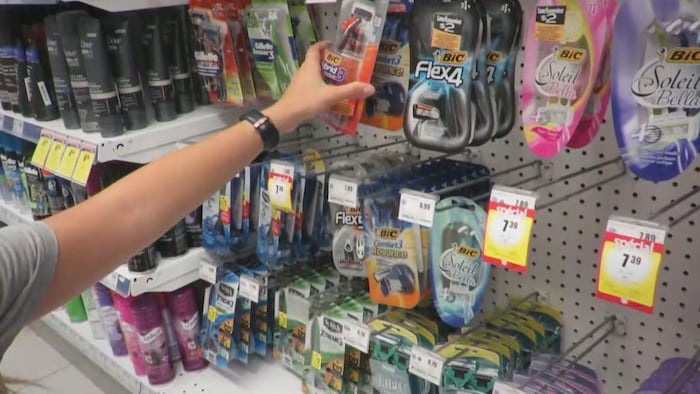 Une jeune femme compare les prix des rasoirs dans une pharmacie.