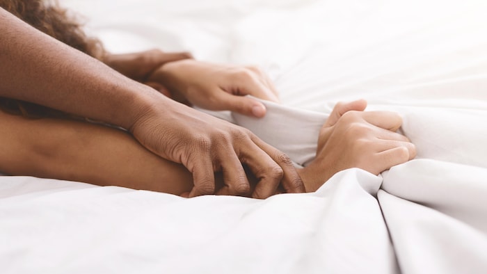Les bras d'un couple d'entrecroisent sur les draps d'un lit. 