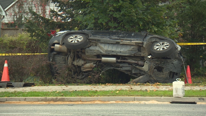 Une voiture noire sur le flanc sur un trottoir.