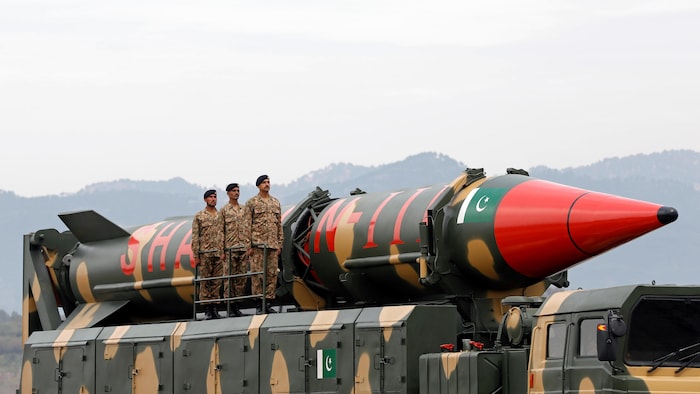 Trois militaires se tiennent à côté d'un grand missile porté sur un camion.