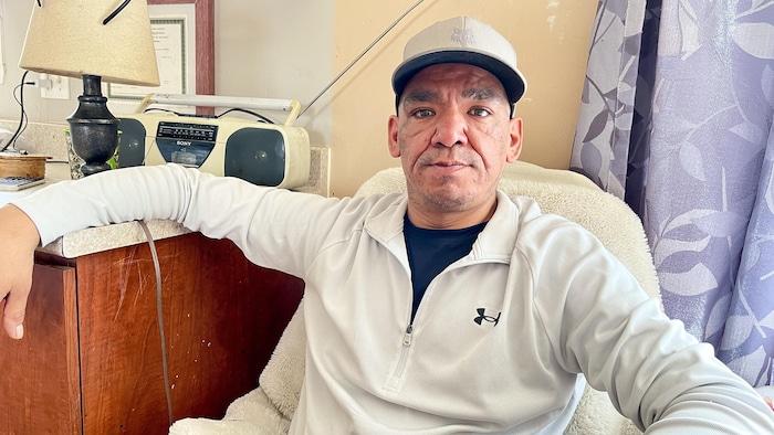 L'homme portant une casquette est assis à la table de la cuisine de sa résidence.