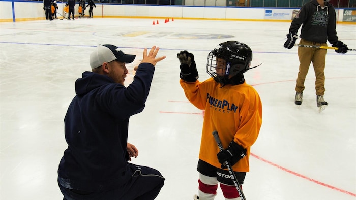 Sheldon Reasbeck sur la glace interagit avec un jeune hockeyeur.