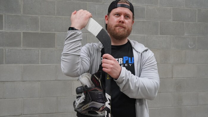Un homme avec une paire de patin et bâton de hockey dans les mains.