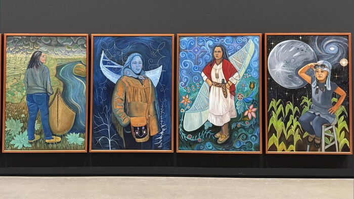 Une série de quatre grandes peintures colorées accrochées côte à côte sur un mur noir.