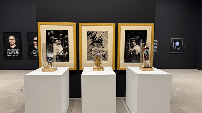 Dans une salle d'exposition, trois portraits en noir et blanc sont accompagnés de sculptures perlées sous cloche.
