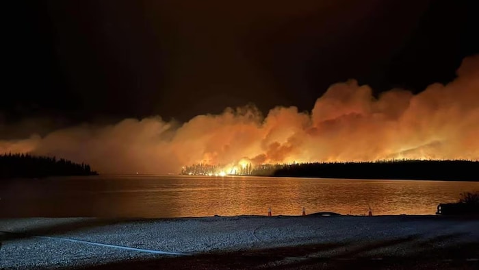Un feu de forêt et de la fumée par-dessus-des arbres brûlants.
