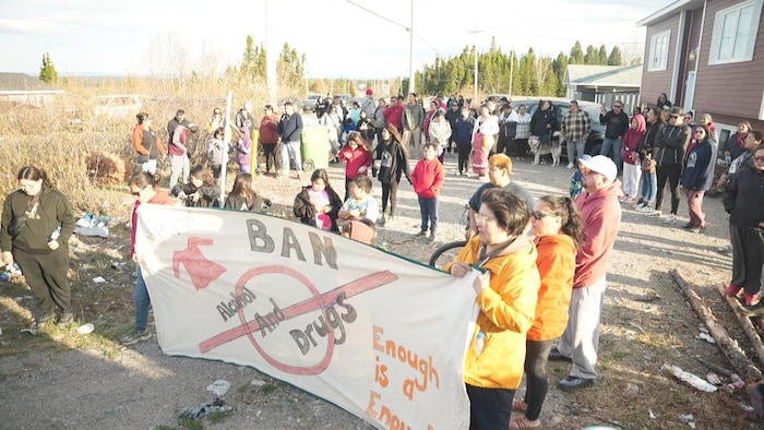 Un groupe de plusieurs dizaines de personnes à l'extérieur. Le groupe à l'avant déploie une longue bannière rectangulaire sur laquelle on a peint un message demandant l'interdiction de l'alcool et des drogues.