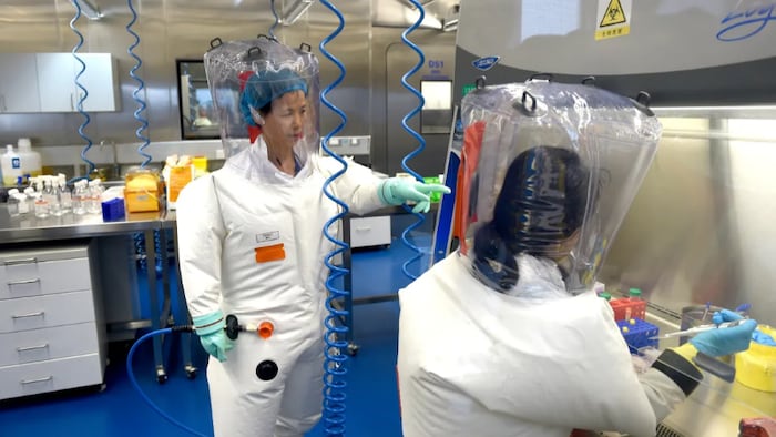 On voit des laborantins vêtus de combinaisons dans un laboratoire qui étudie les pathogènes. Debout, Mme Shi, concentrée sur son travail.