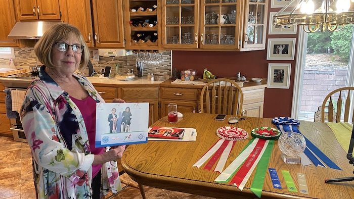 Patti Paquette avec une photo à la main, les rubans gagnés en Italie derrière elle.