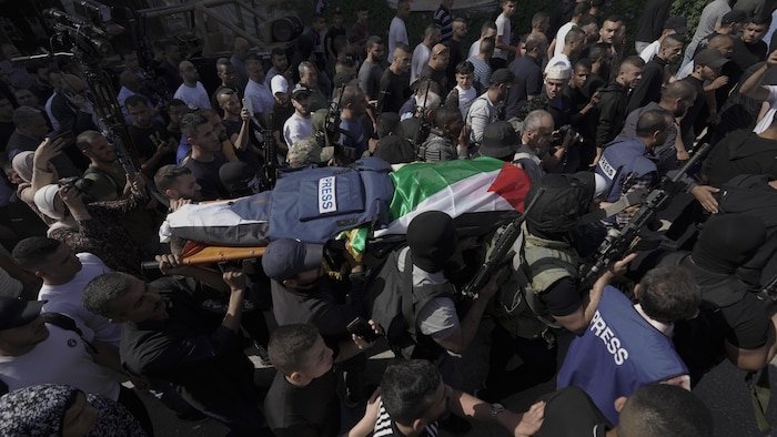 Una multitud lleva una camilla con un cuerpo encima, cubierto con una bandera palestina y un chaleco antibalas. 