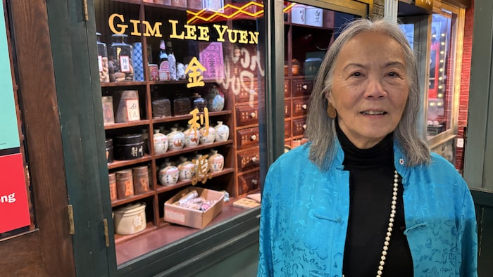 Une femme debout devant la vitrine d'un magasin de plantes traditionnelles.