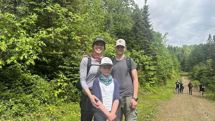 Une famille regarde l'objectif dans la forêt, des personnes marchent au loin sur le sentier.