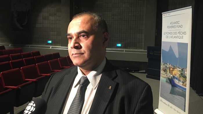 Un homme est debout dans un auditorium avec un micro de Radio-Canada pointé dans sa direction.