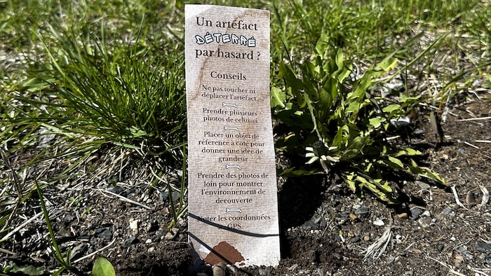 Un papier rectangulaire dans l'herbe qui indique des conseils comme «ne pas toucher ni déplacer l'artéfact».