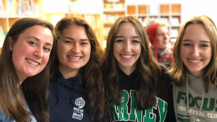 Quatre jeunes femmes souriantes se tiennent les épaules et sourient pour l'objectif.