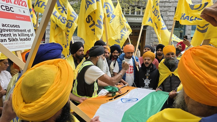 Des manifestants déchirent à l'aide d'une dague le drapeau indien, alors que chacun d'eux brandit des drapeaux du Khalistan, jaune et bleu. 