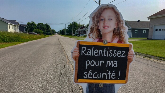 Panneau d'un enfant qui tient un tableau qui dit « Ralentissez pour ma sécurité », au centre d'une rue résidentielle à Saint-Narcisse.