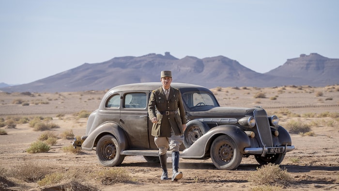 Le général de Gaulle devant une vieille voiture dans le désert. 