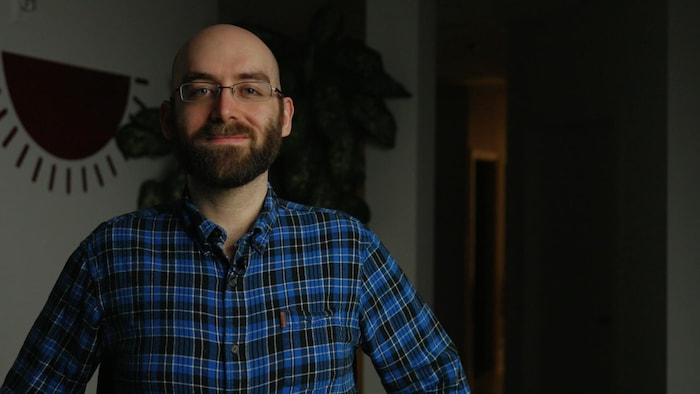 Un homme portant une chemise à carreaux et des lunettes prend la airs dans un bureau.