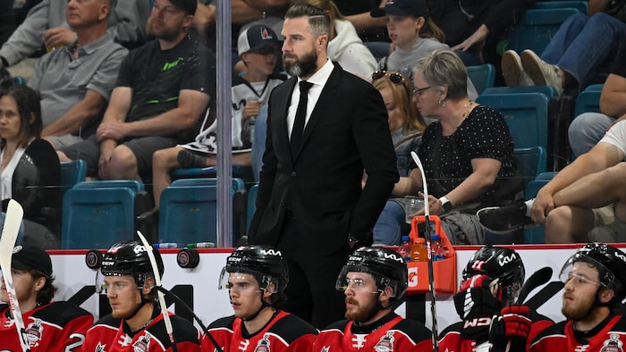 Simon Gagné est debout derrière le banc des Remparts lors d'un match.