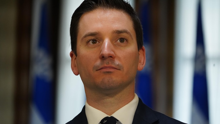 Simon Jolin-Barrette est debout devant des drapeaux du Québec.