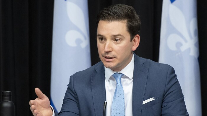 Le ministre Simon Jolin-Barrette lors d'une conférence de presse. Il est assis à une table et parle dans un petit micro.