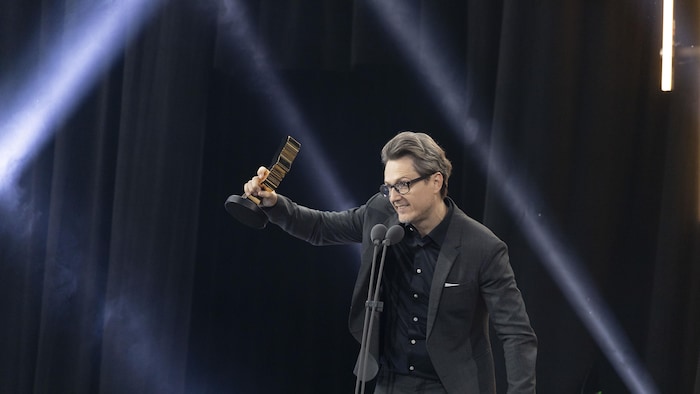 Simon-Olivier Fecteau tient son trophée en signe de victoire sur scène. 