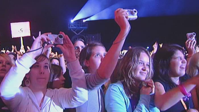 Des gens devant une scène prennent des photos avec de petits appareils numériques.