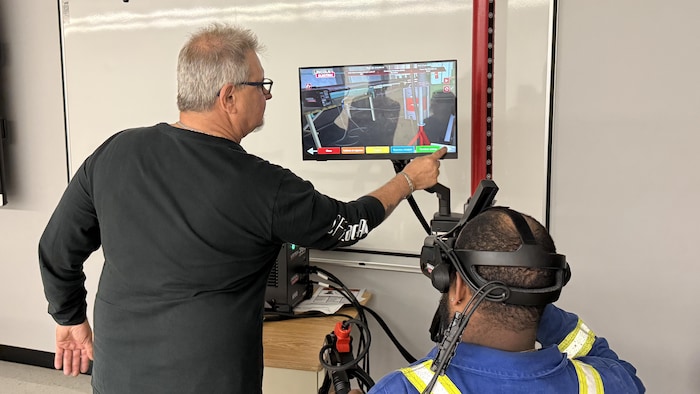 Un élève avec un casque de réalité virtuelle est assis pendant que l'enseignant programme l'écran.