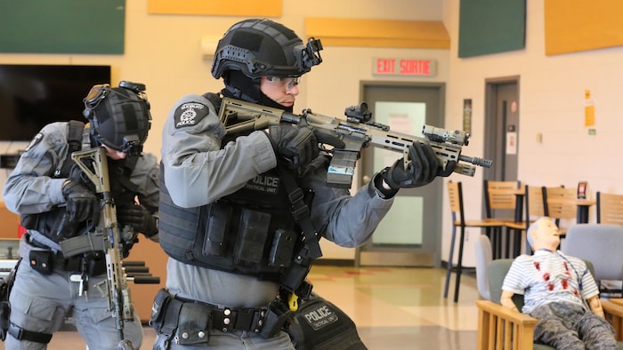 Un agent de police tient une arme dans les mains.
