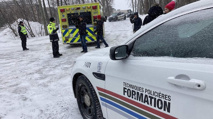 Un véhicule de formation en techniques policières et une ambulance stationnés près d'un boisé en hiver.