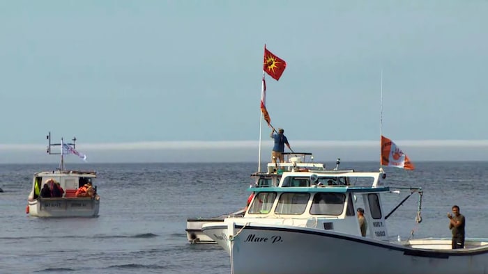A view of flotilla of boats. They took to the water Thursday to haul Sipekne'katik treaty fishery traps. A man is raising a flag, and another on deck is looking at the camera.