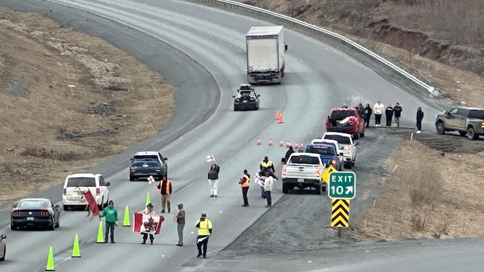 Sur une photo prise en hauteur, des personnes manifestent sur une voie de l'autoroute, bloquant la sortie 10, tandis que des véhicules circulent de l'autre côté de cônes fluorescents posés sur la chaussée. 